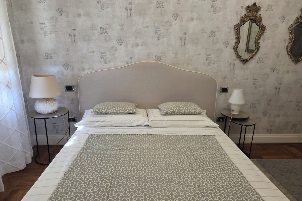 A neatly made bed with patterned bedding, two bedside lamps, and a decorative mirror on the wall.