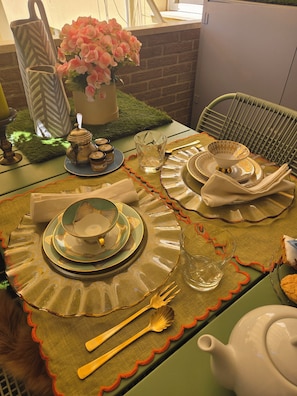 Una mesa de comedor dispuesta con platos, cubiertos, una tetera y un florero con flores.