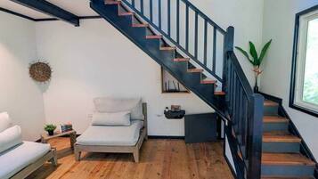 A modern room with a wooden floor, a bed, a small table with a plant, a wall-mounted shelf, and a staircase with black railings.
