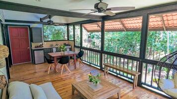 A spacious room with a wooden floor, a dining table with chairs, a sofa, a bench, and a ceiling fan.