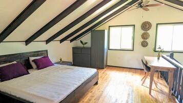A bedroom with a bed, a desk, a chair, a ceiling fan, and a window.
