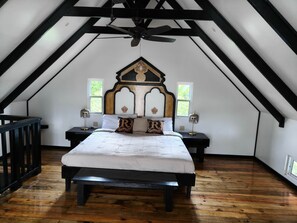 Ein Schlafzimmer mit schrägen Wänden, einem Bett mit weißer Bettwäsche, zwei Nachttischen mit Lampen und einer hölzernen Bank.