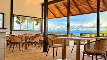 Un espacio de comedor al aire libre con mesas y sillas de madera, amplias ventanas y vistas al cielo y las nubes.
