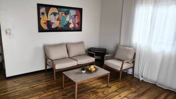 Uma sala de estar com sofá, poltrona, mesa de centro e um quadro na parede.