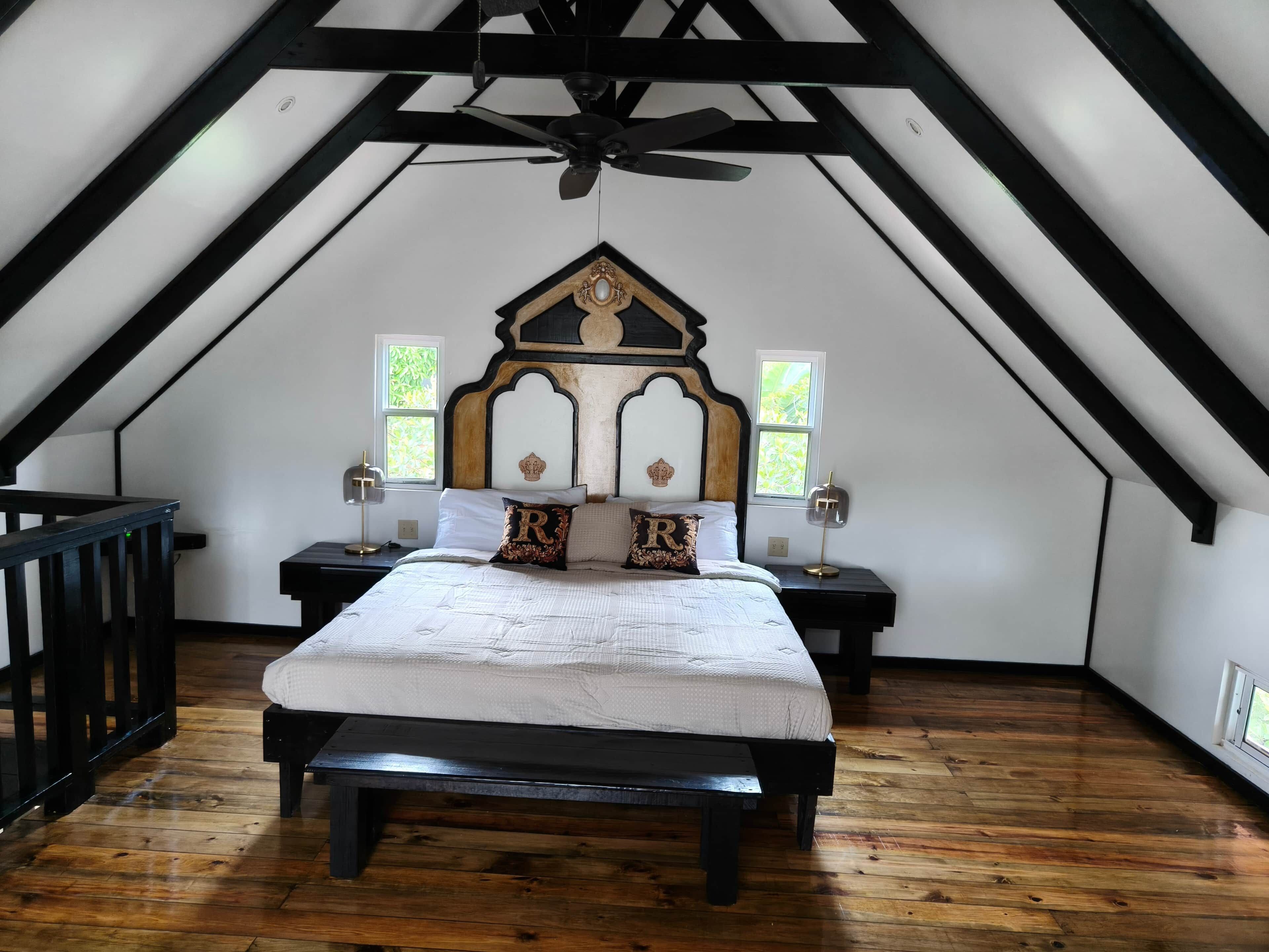 Une chambre avec un plafond en pente, un lit avec une literie blanche, deux tables de chevet avec des lampes et un banc en bois.