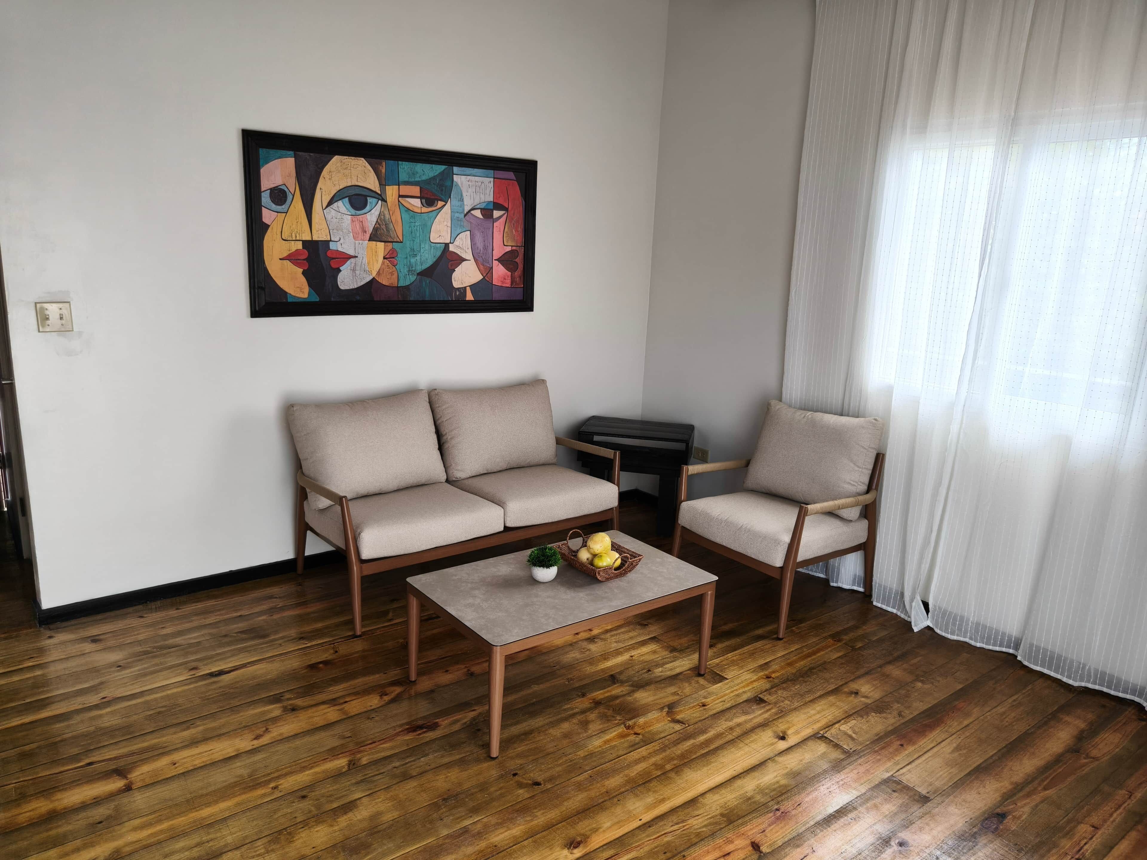 Een woonkamer met een bank, fauteuil, salontafel en een schilderij aan de muur.