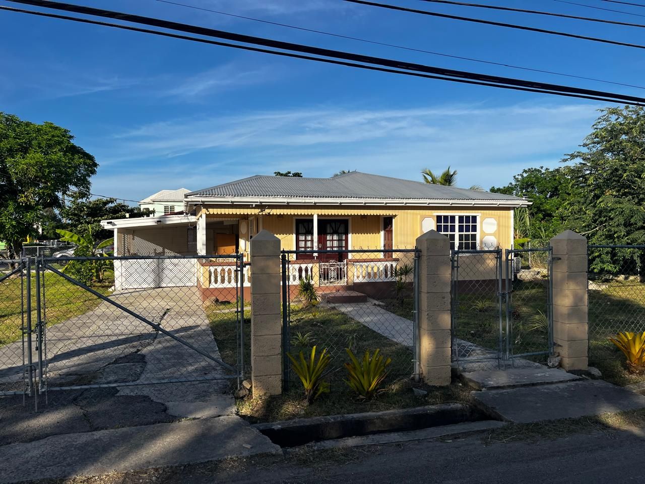 A residential house with a fenced driveway, a covered porch, and a small garden area.