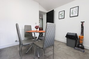 A dining area with a table and chairs, a trash bin, and a vacuum cleaner. - Stylish and comfortable apartment in Cardiff (Cardiff)