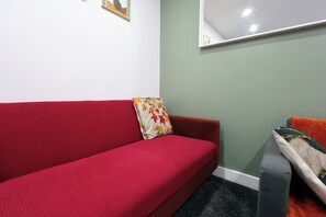 A red sofa with a floral pillow, a grey armchair, and a small table with a white tablecloth. - Stylish and comfortable apartment in Cardiff (Cardiff)