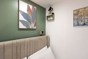 A bedroom with a bed, a wall-mounted shelf with decorative items, and two framed artworks. - Stylish and comfortable apartment in Cardiff (Cardiff)