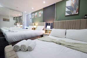 Habitació d'hotel amb diversos llits, una finestra gran amb persianes i obres d'art a les parets.