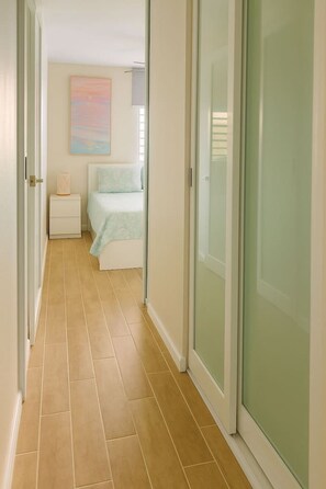 A hallway with a bed, a nightstand, and a painting on the wall. - Costa Córcega 5A | Beachfront, Pool & Beach Access (Rincón)