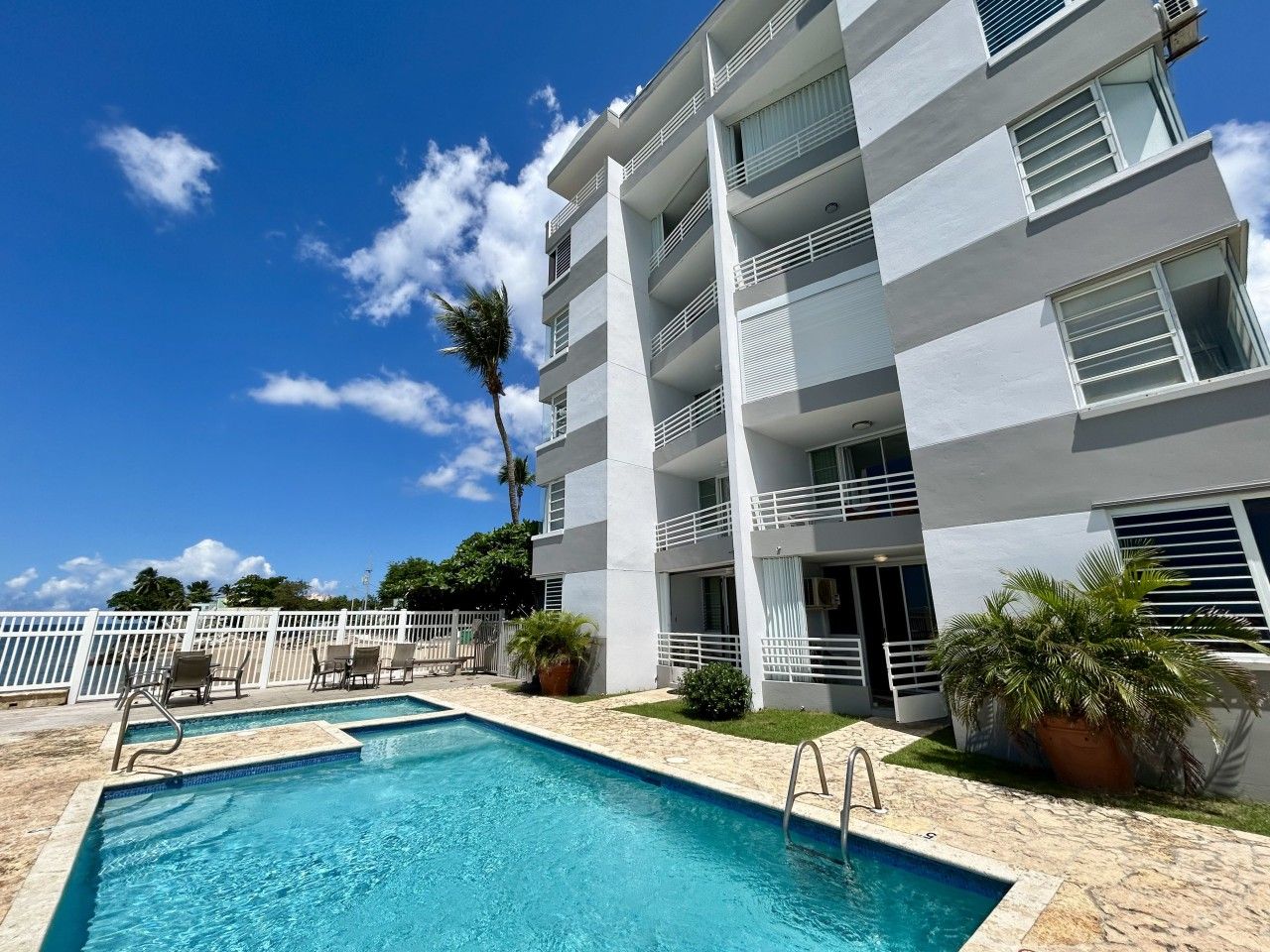 A hotel with a pool, white balconies, and a clear blue sky.