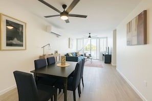 A modern living room with a dining area, ceiling fans, and large windows. - Costa Córcega 5A | Beachfront, Pool & Beach Access (Rincón)