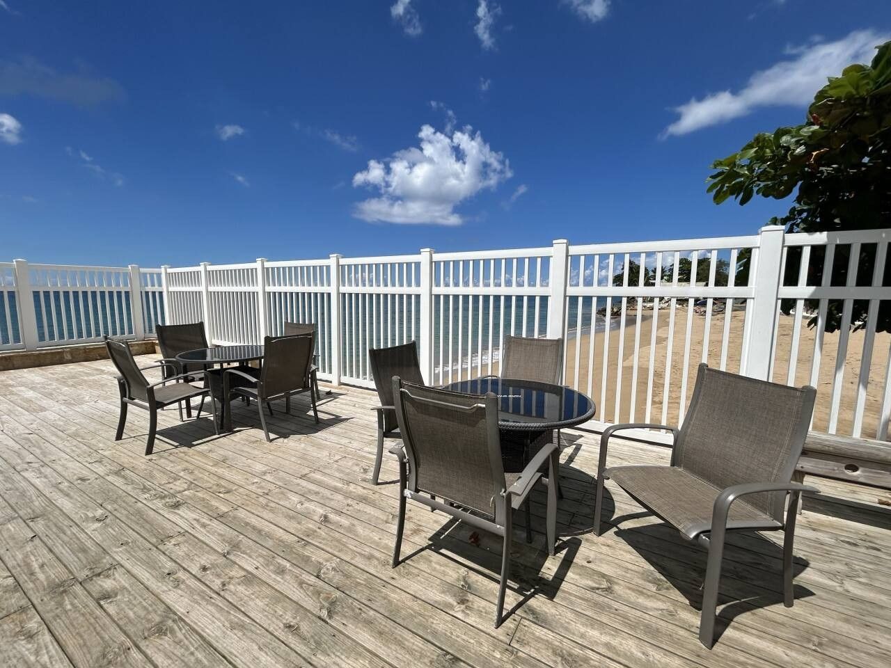 An outdoor deck with a round table and chairs, surrounded by a white fence.