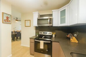 A compact kitchen with a microwave, oven, and stove. There is a dining area visible in the background. - Costa Córcega 5A | Beachfront, Pool & Beach Access (Rincón)