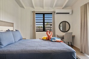 Une chambre d’hôtel comprenant un lit, un bureau, un appareil de climatisation, une fenêtre avec des volets et un miroir décoratif.