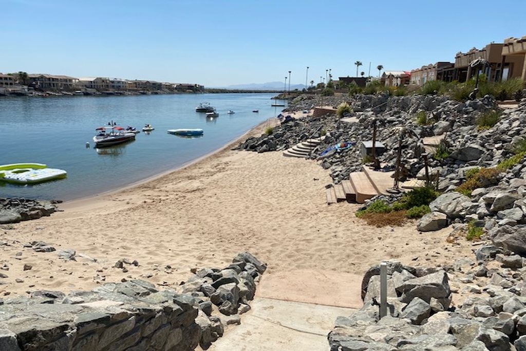 A beach with boats, a rocky shoreline, and buildings in the background.