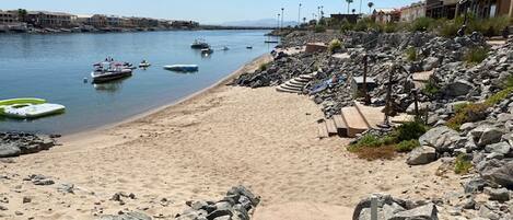 A beach with boats, a rocky shoreline, and buildings in the background.