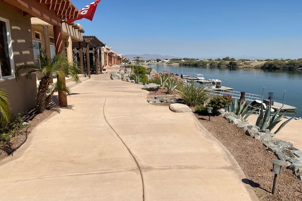 A concrete pathway leading to a building with a flag, a body of water, and boats.