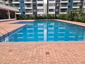 A swimming pool with a tiled edge, surrounded by a brick patio. - Modern Makumbi Park Studio Near JKIA & SGR (Nairobi)