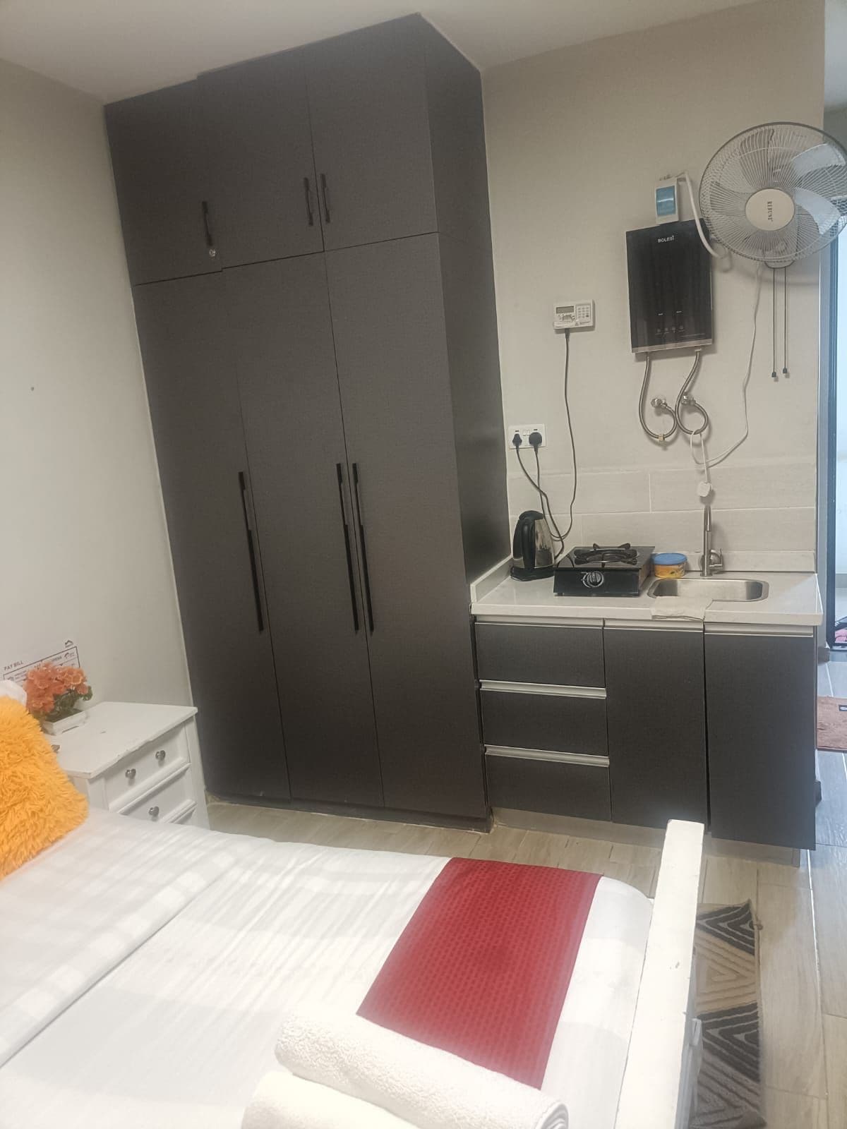 A bedroom with a bed, a wardrobe, a bedside table, a nightstand, and a wall-mounted fan.