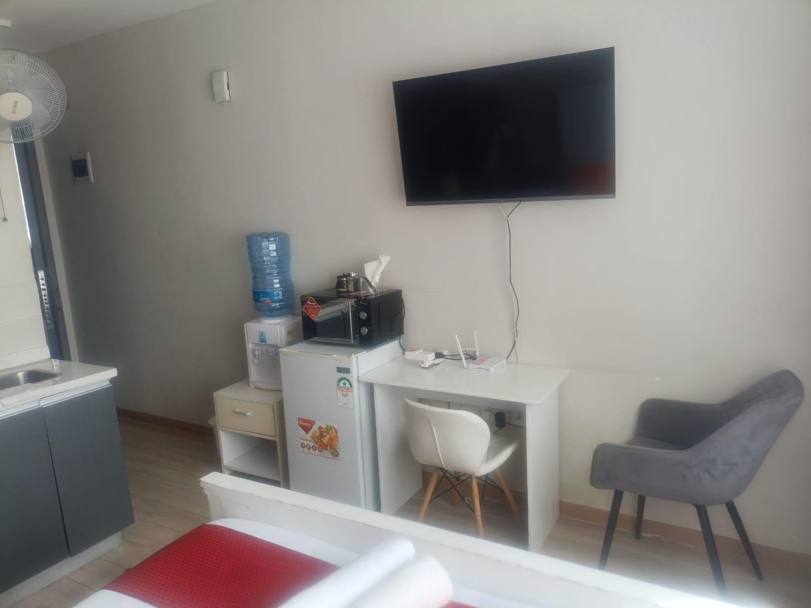A hotel room with a bed, a desk, a chair, a television, a water dispenser, a microwave, and a refrigerator.