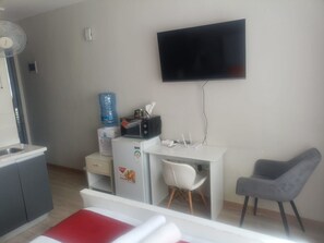 Ein Hotelzimmer mit Bett, Schreibtisch, Stuhl, Fernseher, Wasserspender, Mikrowelle und Kühlschrank.