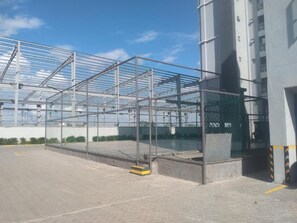 Ein Gewächshaus mit Metallrahmen und Glasfeldern neben einem Gebäude mit Betonfundament und einer senkrechten Metallstütze.
