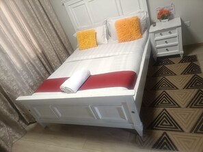 A neatly made bed with a white headboard, two pillows, a rolled white towel, and a red blanket. - Modern Makumbi Park Studio Near JKIA & SGR (Nairobi)