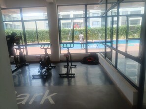 Ein Fitnessraum mit Trainingsgeräten und großen Fenstern mit Blick auf ein Schwimmbecken.