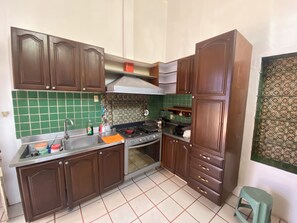 A kitchen with brown cabinets, a gas stove, a sink, and a green tiled backsplash. - HOSTEL & LOFTS CASA LUMA (Guadalajara)
