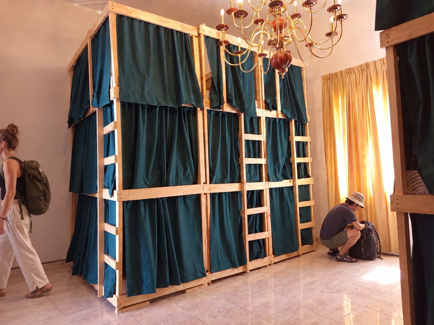 A room with a bunk bed, a chandelier, and a window with curtains.