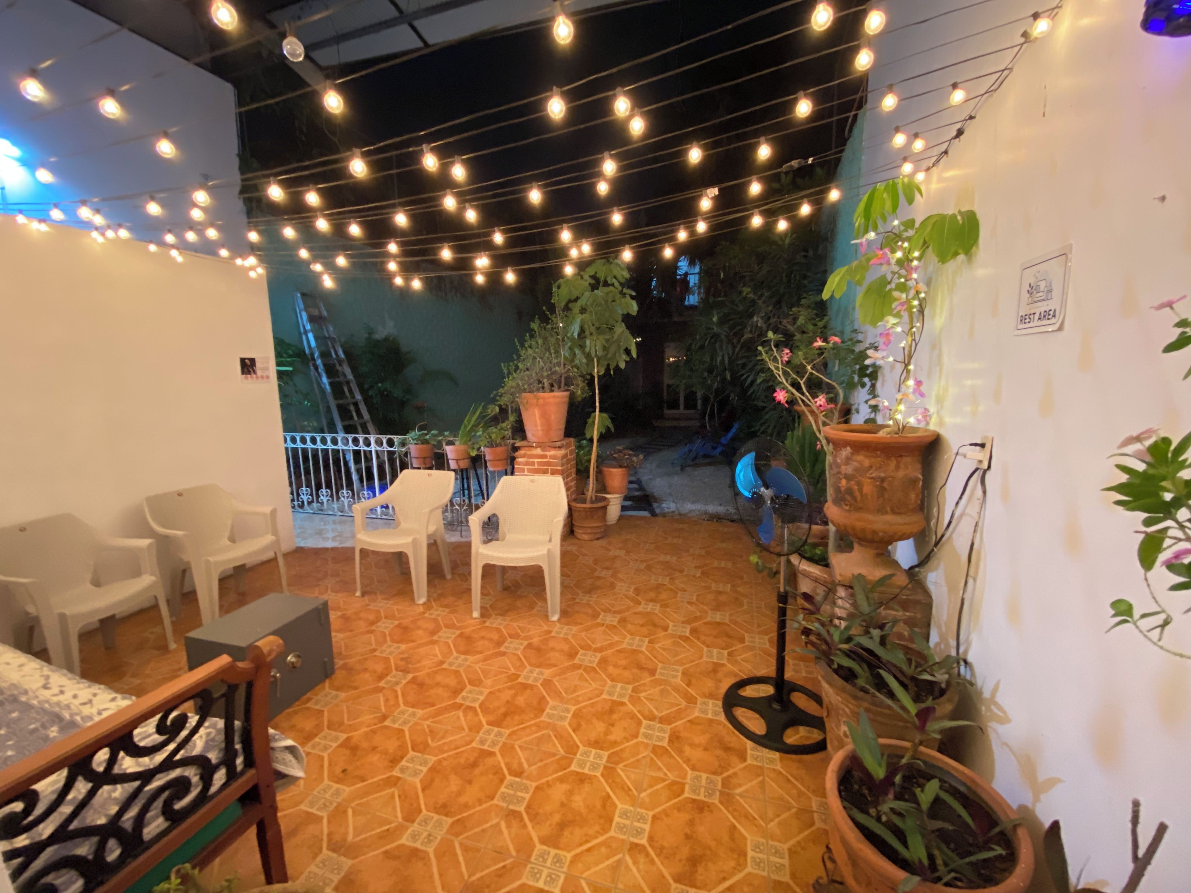 An outdoor seating area with chairs and tables, surrounded by potted plants and string lights.