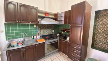 A compact kitchen with brown cabinets, a stainless steel sink, a gas stove, and a tiled backsplash.