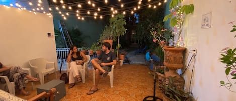 Un espacio de estar al aire libre cubierto con luces colgantes, plantas en macetas y un letrero que indica un área de descanso.