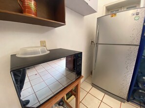 A kitchen with a microwave on a black countertop, a refrigerator with decorative stickers, and a shelf with a red mug. - HOSTEL & LOFTS CASA LUMA (Guadalajara)