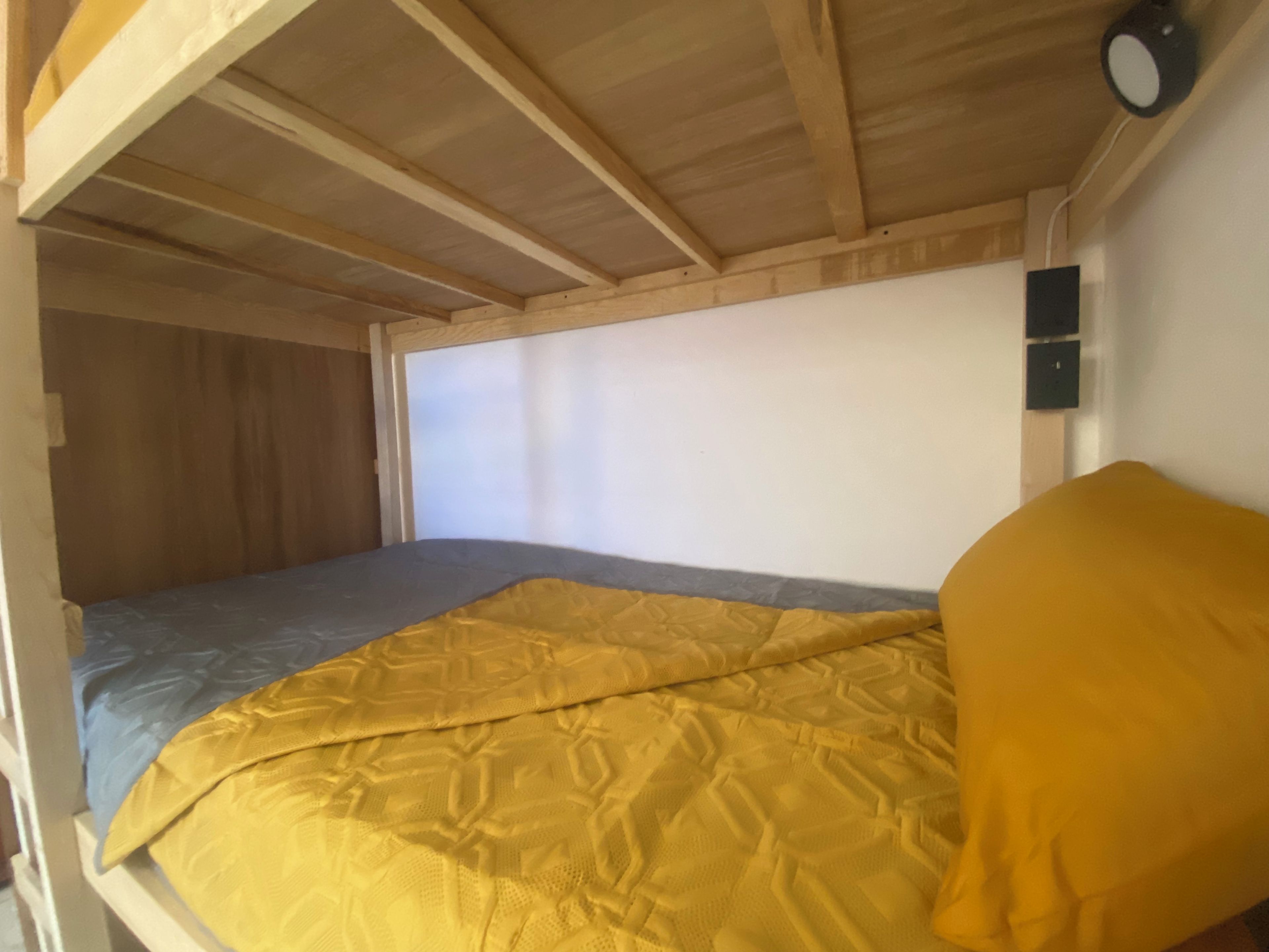 A bunk bed with a yellow blanket and a grey mattress.