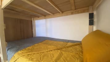 A bunk bed with a yellow blanket and a grey mattress.
