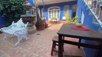 Un patio con suelo de baldosas, un banco blanco, una mesa de madera y plantas en macetas.