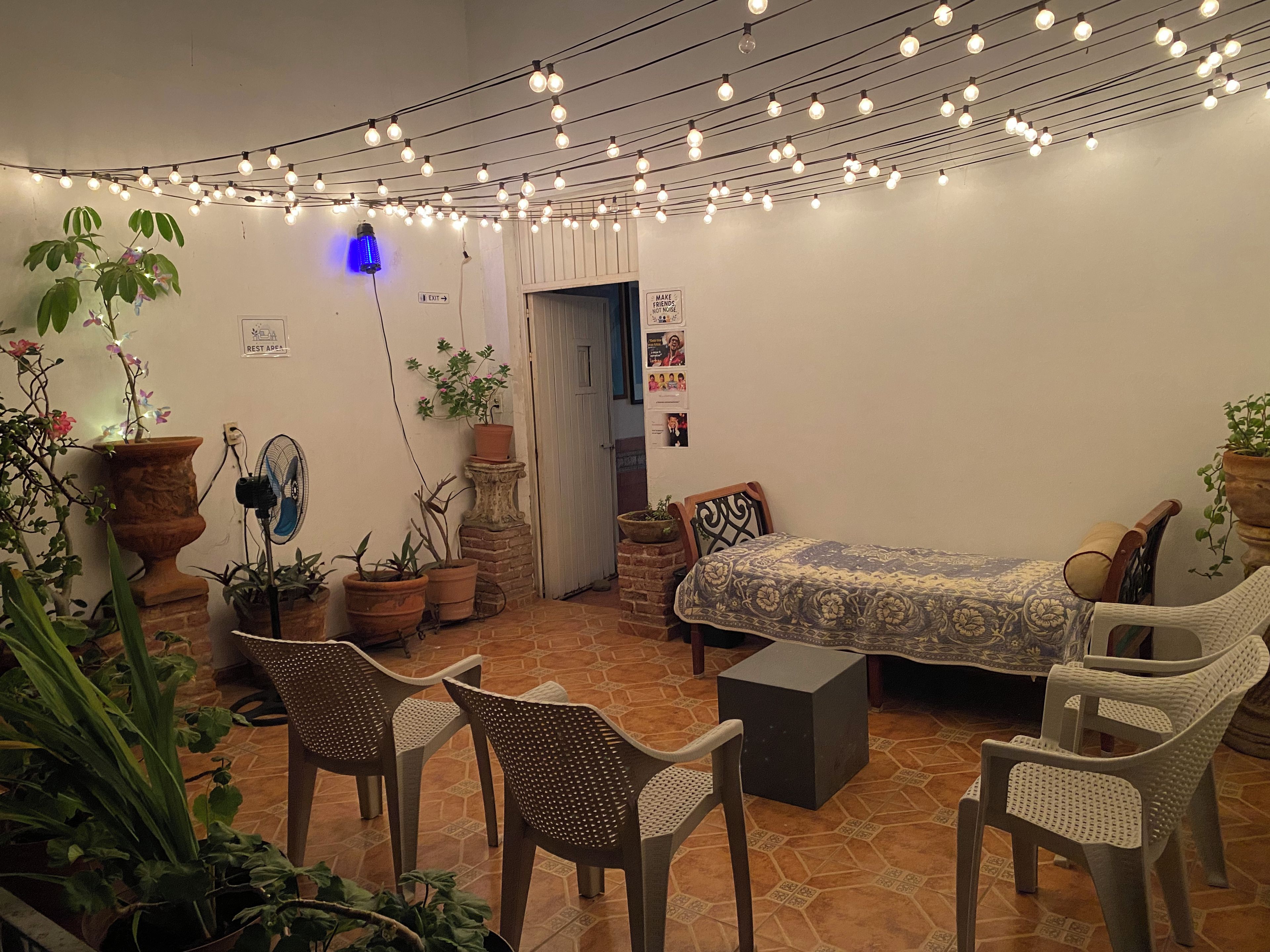 A cozy room with a bed, chairs, and potted plants. There is a sign indicating a rest area and a door leading outside.