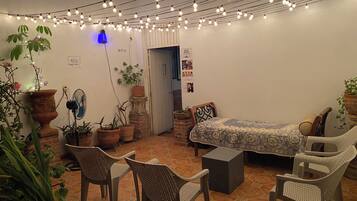 A cozy room with a bed, chairs, and potted plants. There is a sign indicating a rest area and a door leading outside.