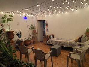 A cozy room with a bed, chairs, and potted plants. There is a sign indicating a rest area and a door leading outside. - HOSTEL & LOFTS CASA LUMA (Guadalajara)