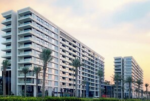 A multi-story residential building with balconies, palm trees, and a clear sky. - Delightful 2-bedroom apartment with AC in Marassi (Muharraq Governorate)