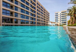 Hotel com vários andares, piscina e céu claro.
