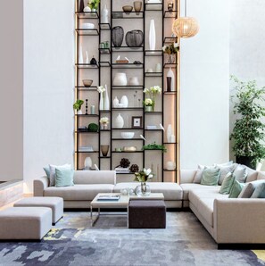 A modern living room with a sectional sofa, a coffee table, and a built-in bookshelf filled with decorative items. - Delightful 2-bedroom apartment with AC in Marassi (Muharraq Governorate)