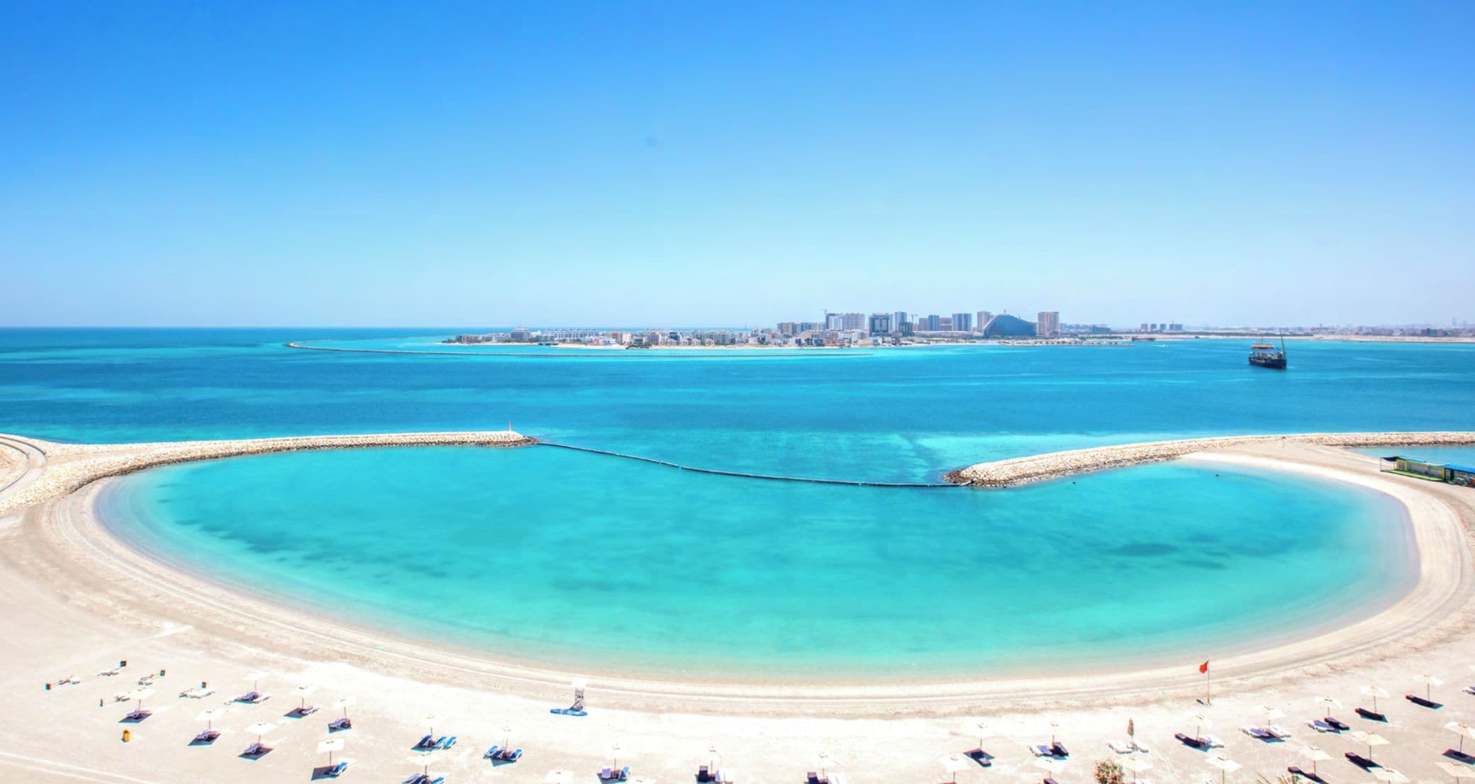 Une plage côtière offrant une vue dégagée sur les gratte-ciel d’une ville en arrière-plan.
