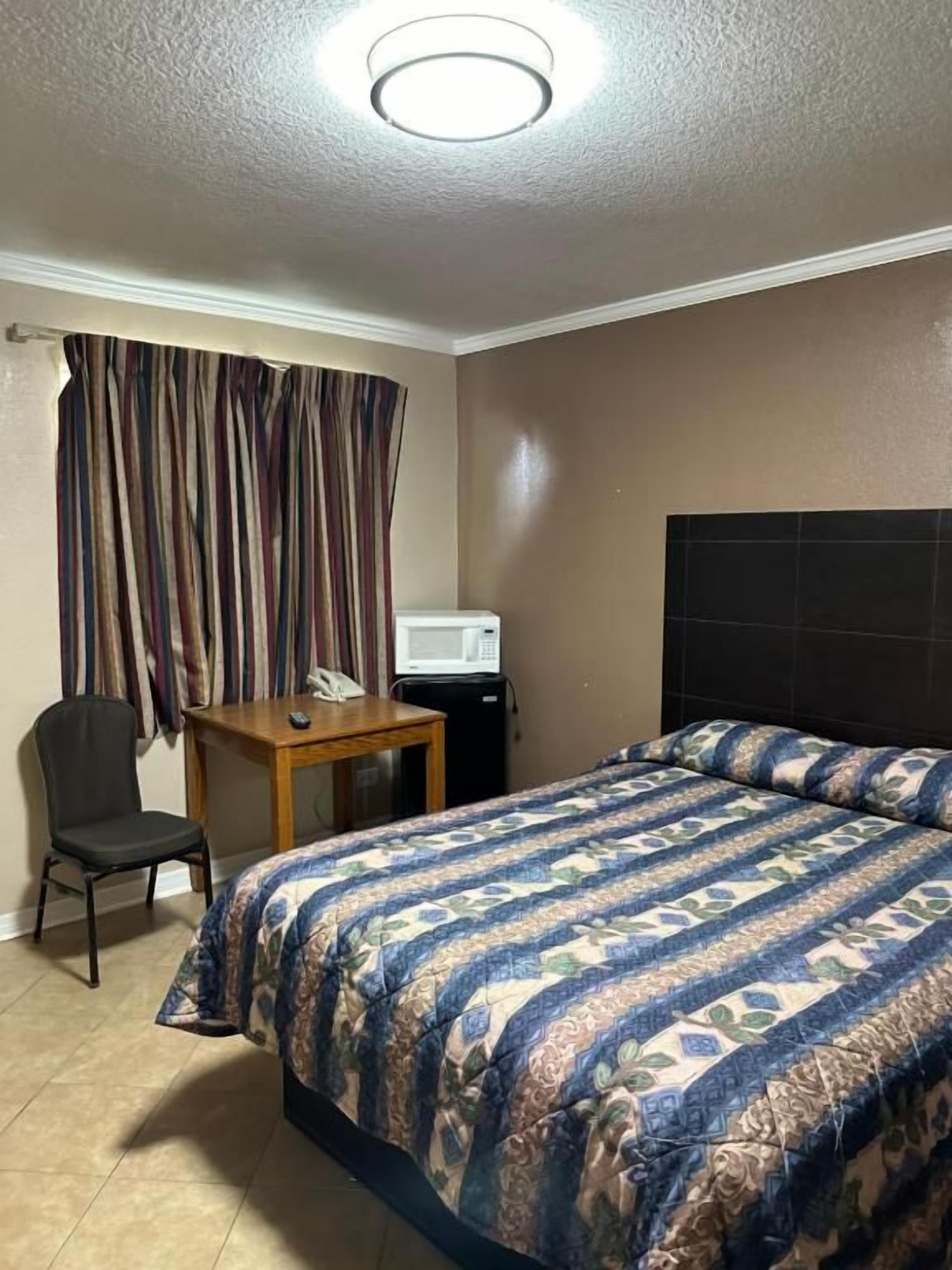 A hotel room with a bed, a desk, a chair, a telephone, and a television.