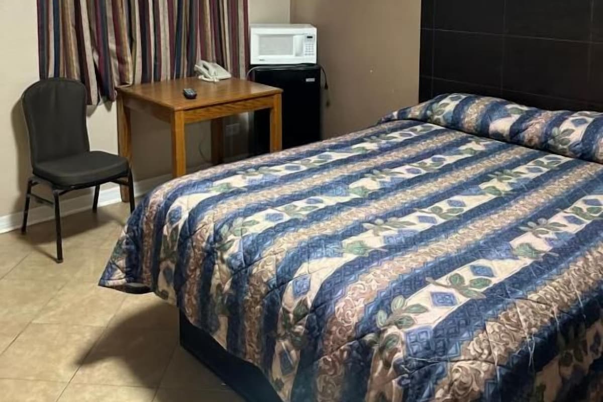 A hotel room with a bed, a desk, a chair, a telephone, and a television.