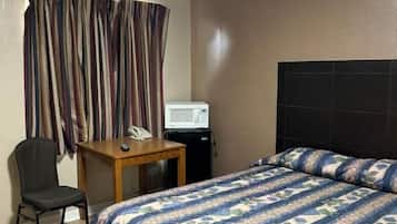 A hotel room with a bed, a desk, a chair, a telephone, and a television.